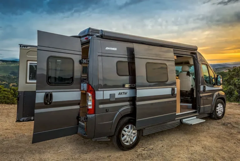 Hymer Aktiv with side and rear doors open at a dirt campsite at sunset